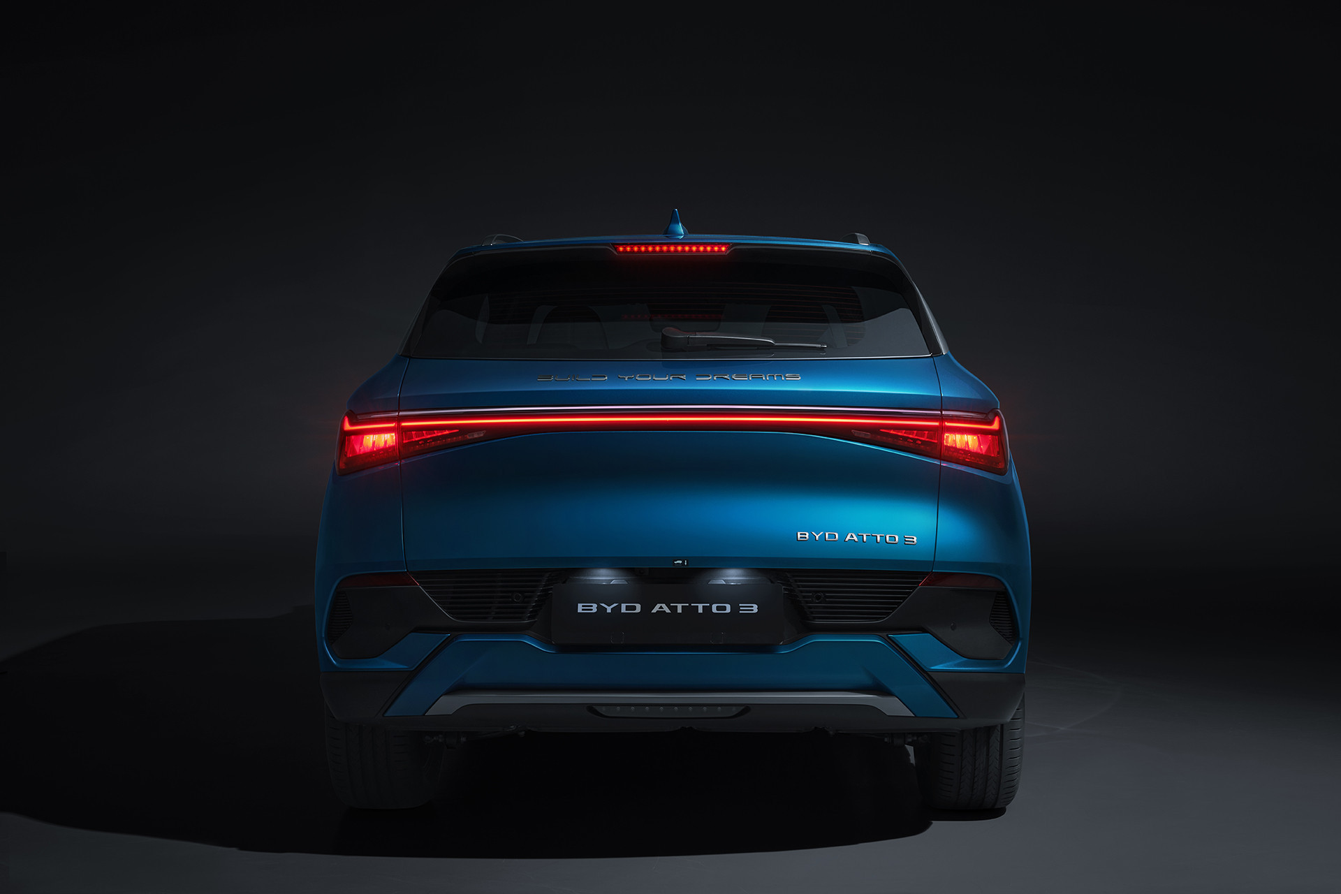 A photograph of a Surfing Blue BYD Atto 3 from the rear in a darkened environment, highlighting the rear brake light design