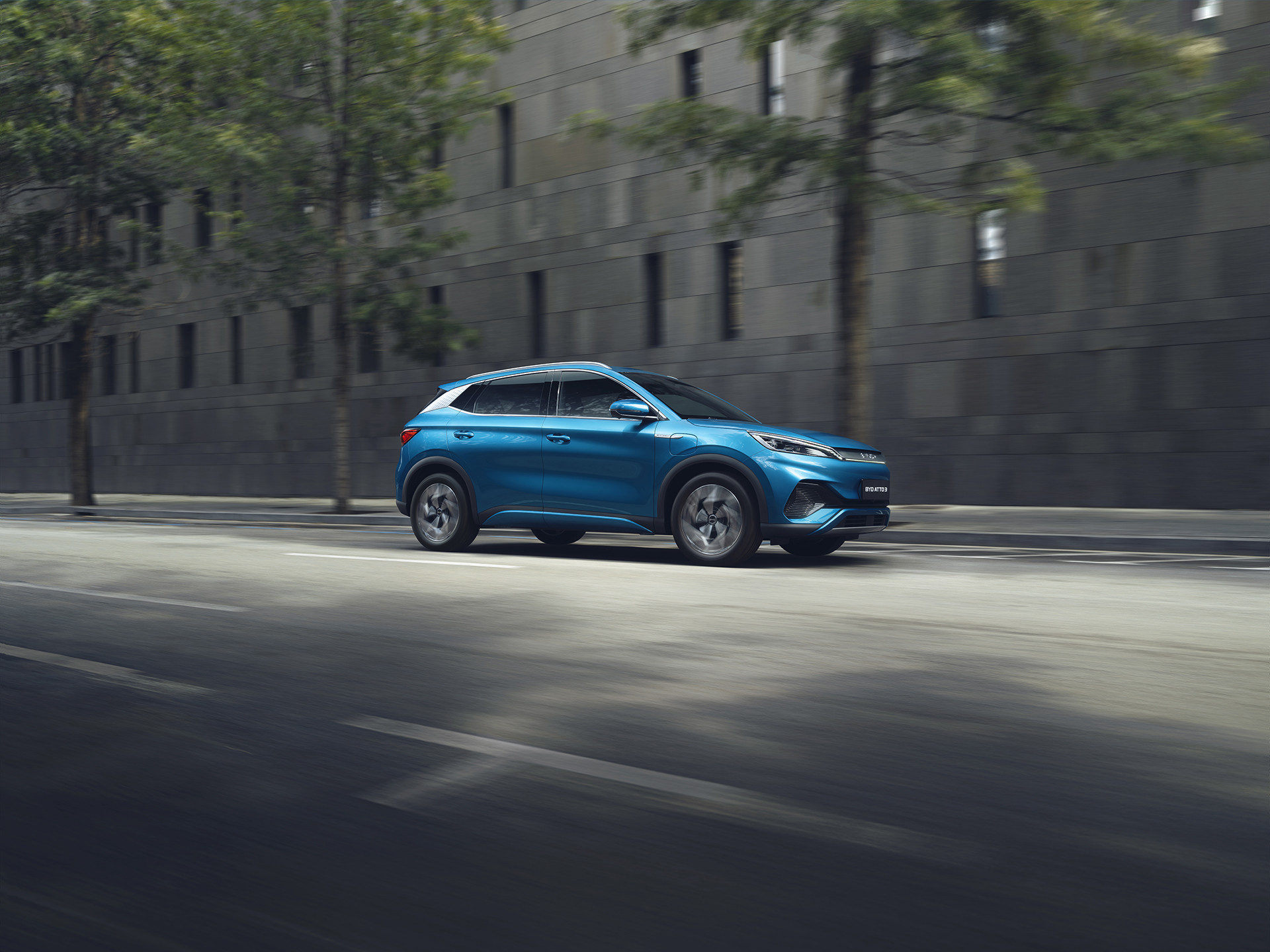 A photograph of a Surfing Blue BYD Atto 3 driving through a city street